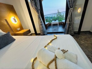 Habitación de hotel con cama, mesita de noche, lámpara de pared y vistas al exterior a través de cortinas abiertas.