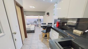 Una cocina moderna con encimera negra, horno empotrado y fregadero. Hay una zona de comedor con mesa y sillas, además de un balcón con vistas.