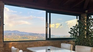 Un comedor con una mesa y sillas, ventanas amplias con vistas al paisaje y techo de madera.