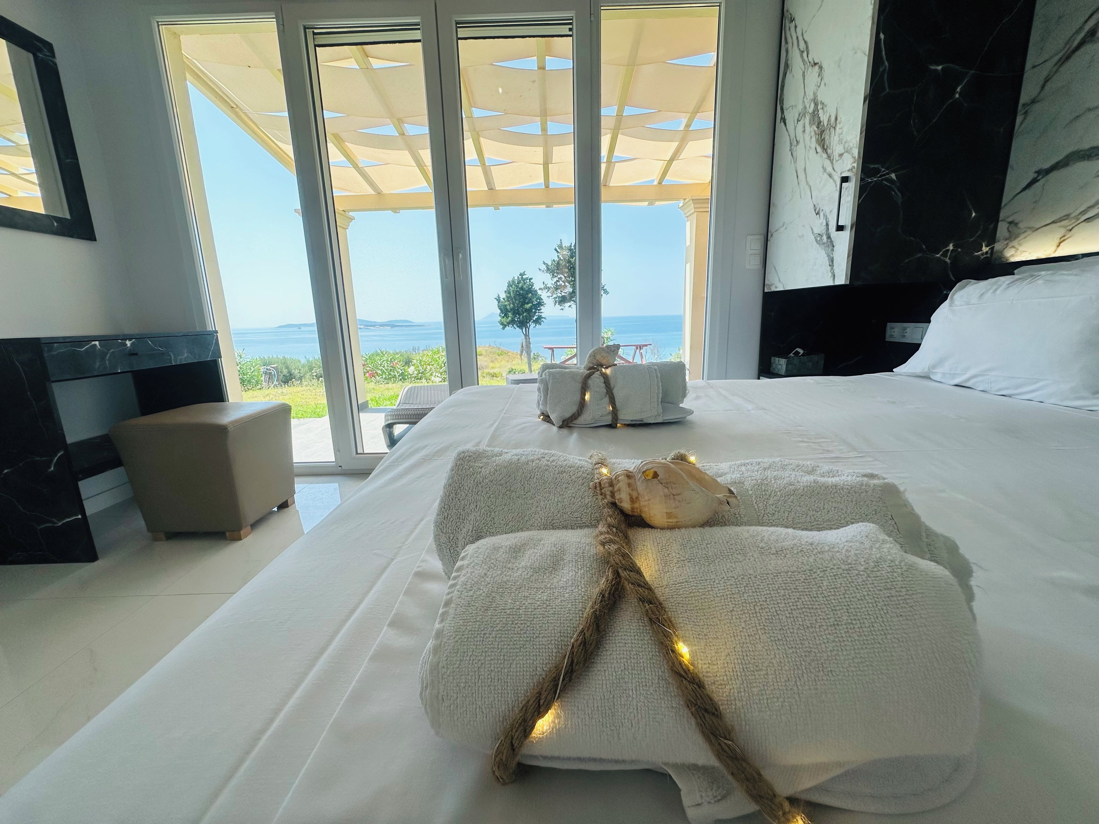 Quarto com uma cama grande, mesa de cabeceira, parede de mármore e vista para o mar.