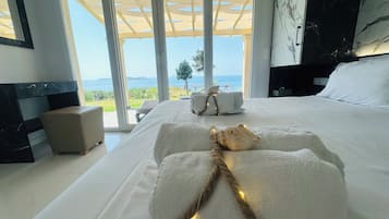 Quarto com uma cama grande, mesa de cabeceira, parede de mármore e vista para o mar.