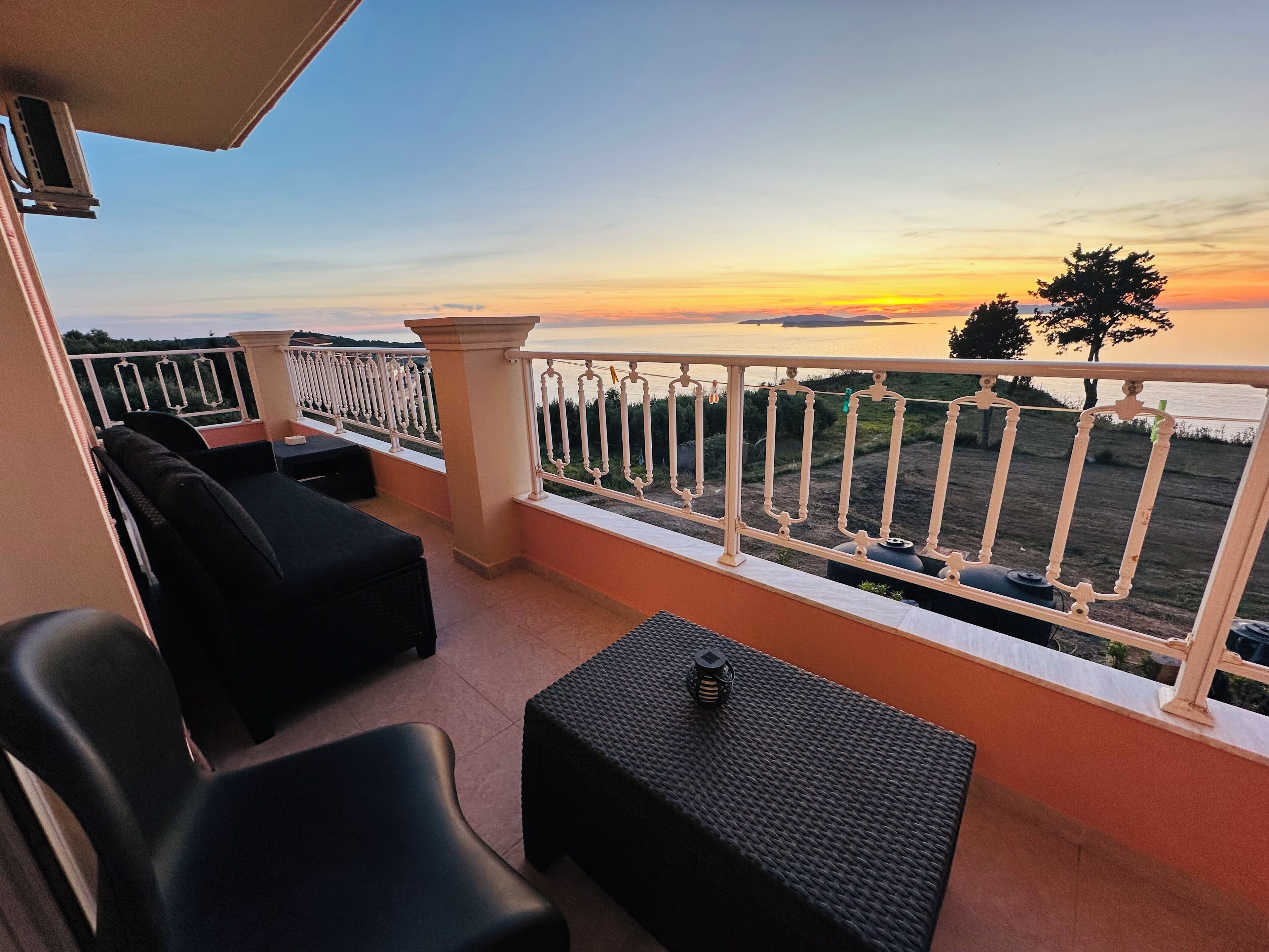 Ein Balkon mit Sitzgelegenheit und Blick auf den Sonnenuntergang über dem Wasser.