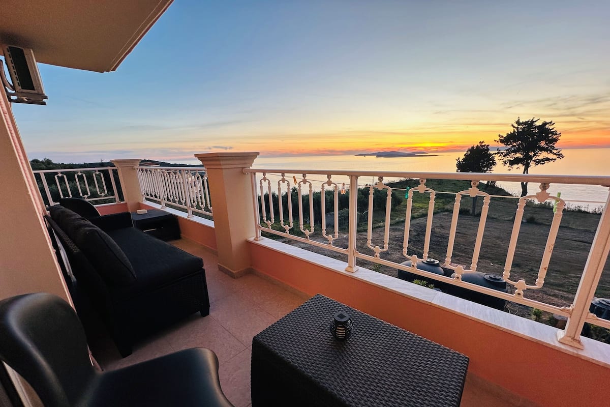 Ein Balkon mit Sitzgelegenheit und Blick auf den Sonnenuntergang über dem Wasser.