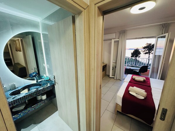 Een hotelkamer met een bed, een badkamer met een wastafel en spiegel, en een balkon met uitzicht.