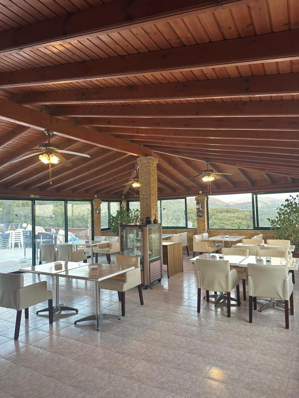 Ein geräumiger Innenbereich zum Essen mit hohen Decken und großen Fenstern, die einen Blick ins Freie ermöglichen.