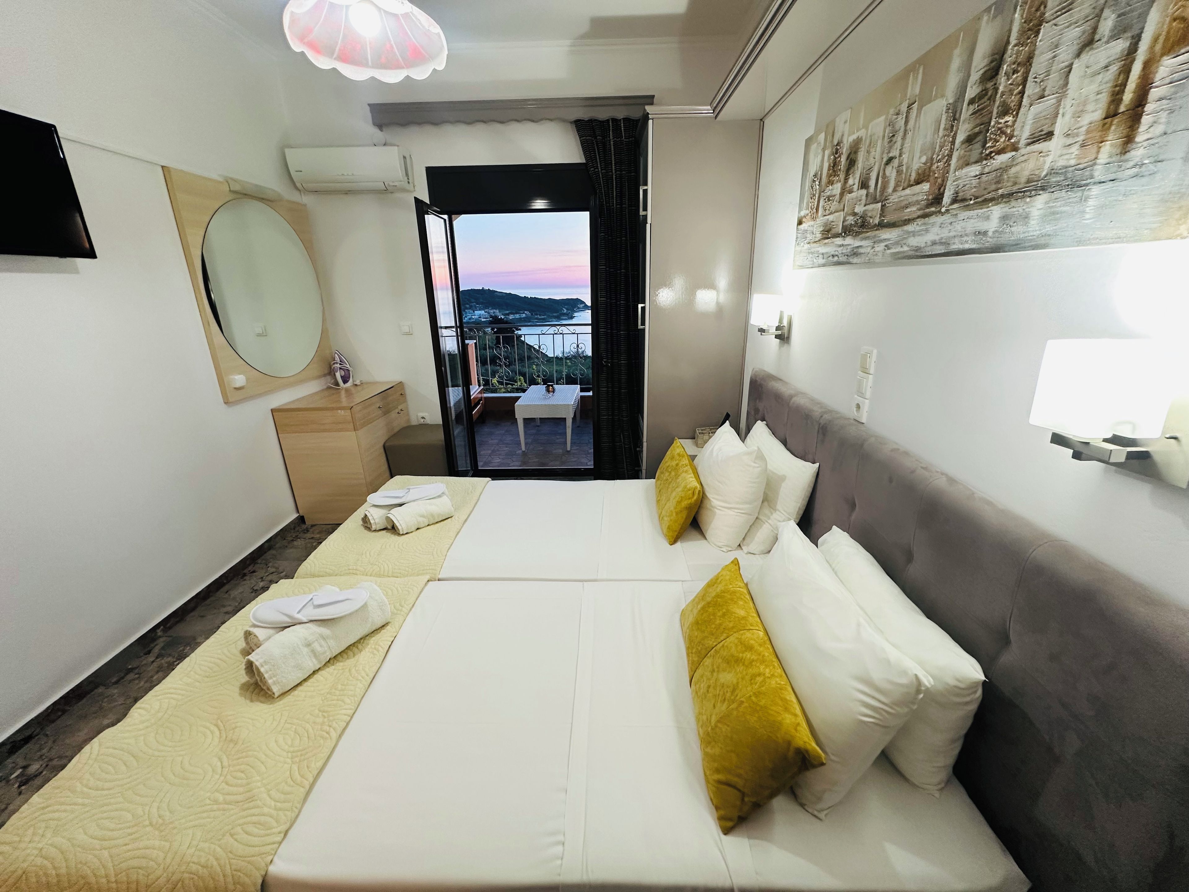 A hotel room with a bed, a bedside table, a mirror, a window with a view, and a ceiling fan.