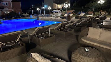 Un espace aménagé au bord de la piscine, avec des chaises longues et une piscine éclairée la nuit.