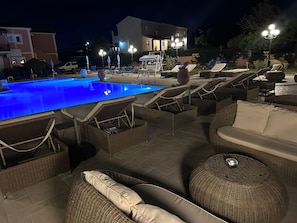 A poolside area with lounge chairs and a swimming pool at night. - Nikos Apartments Corfu (Corfu)