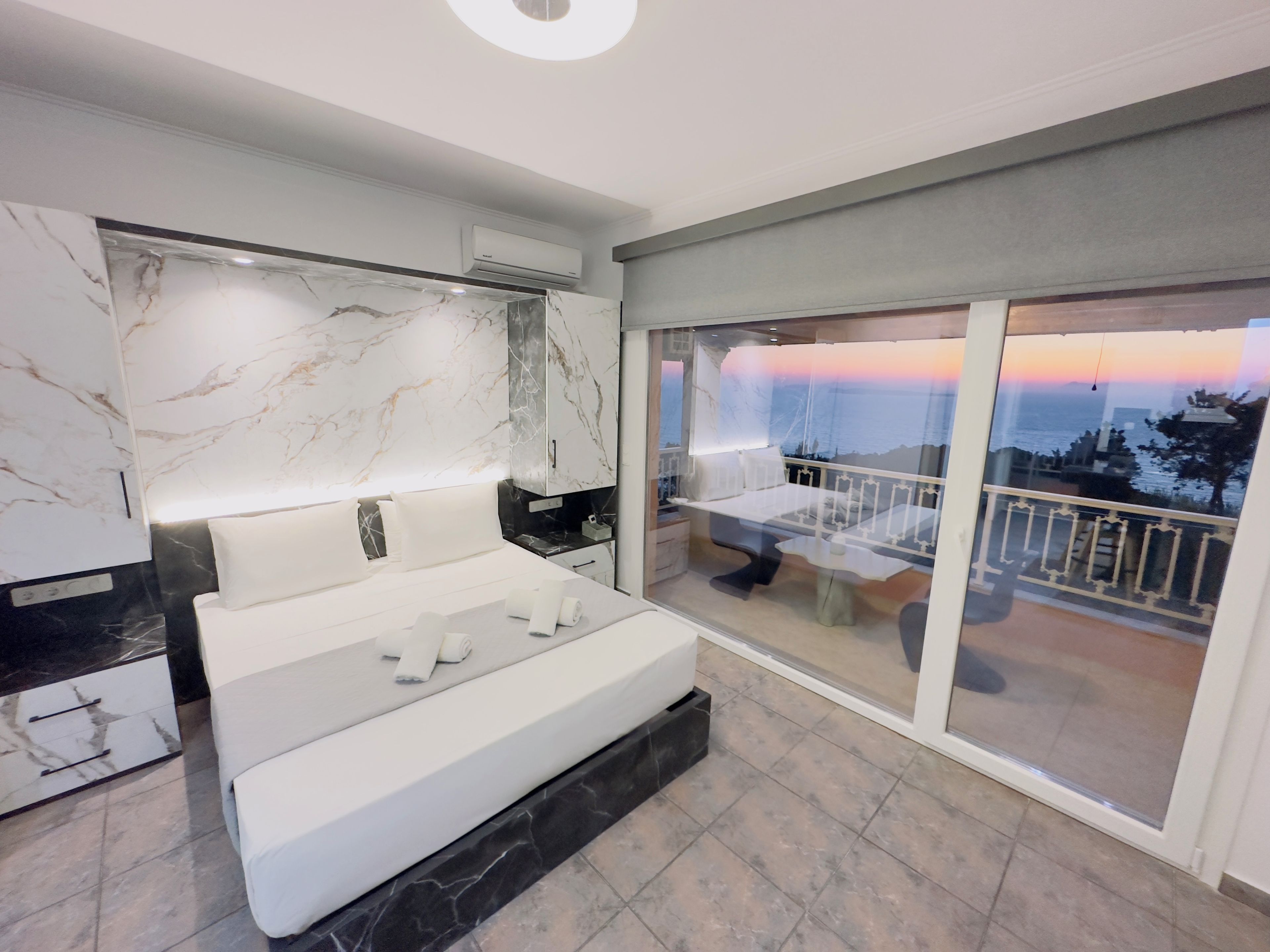 Un dormitorio moderno con una cama grande, una pared de mármol y un balcón con vistas.