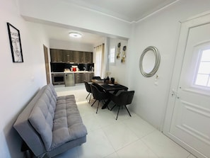 Un appartamento moderno con un divano grigio, un tavolo da pranzo con sedie, una cucina con mobili scuri e una porta bianca.