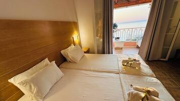 Habitación de hotel con dos camas, cabecero de madera, mesita de noche y vista al mar desde un balcón.