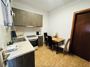 A compact kitchen with a stove, sink, and a dining area with two chairs and a table. - Nikos Apartments Corfu (Corfu)