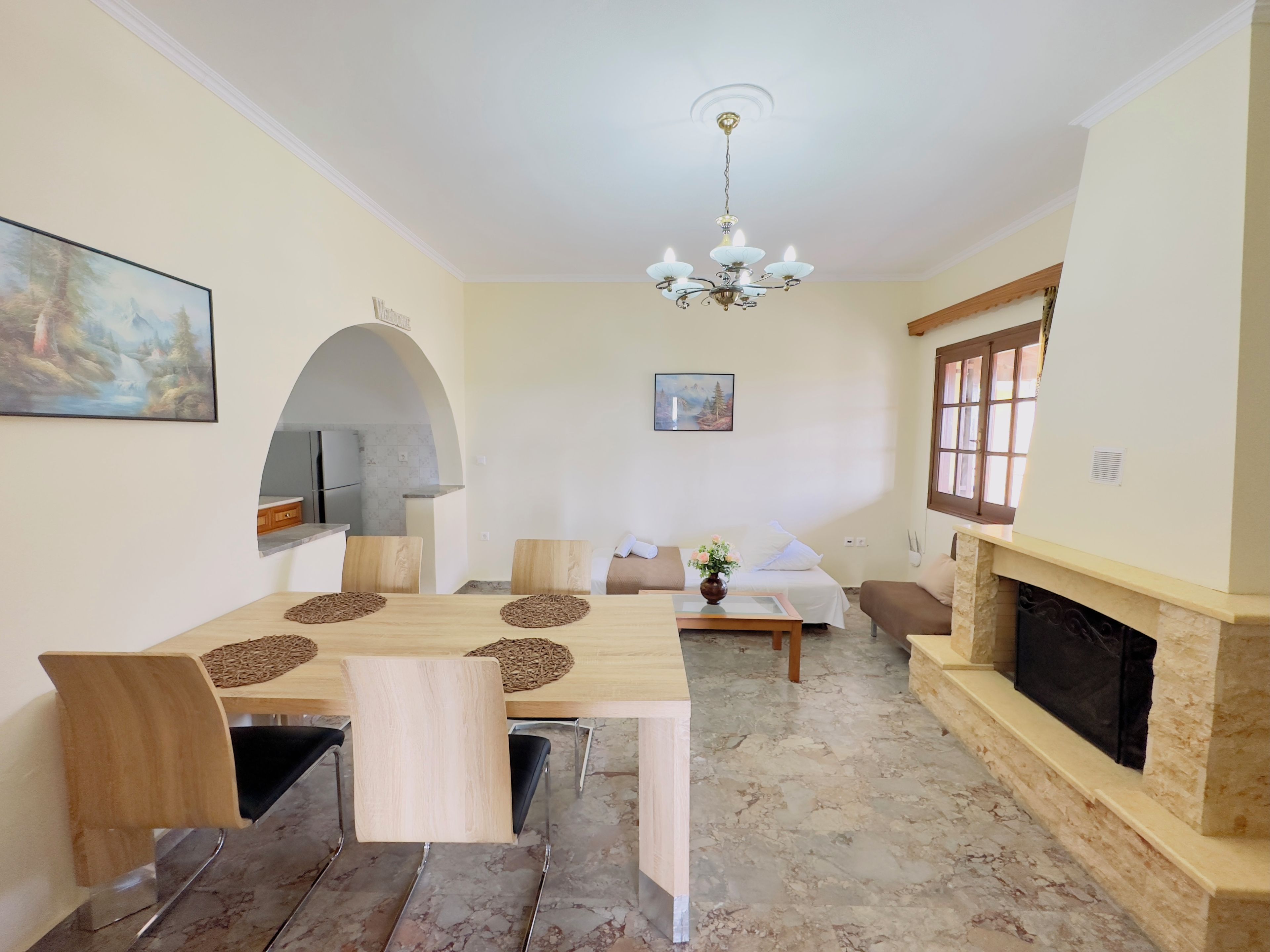 Een eetruimte met een marmeren vloer, houten stoelen, een tafel met placemats, een kroonluchter, een open haard en een schilderij aan de muur.