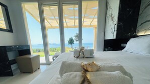 Un dormitorio con una cama grande, una mesita de noche, una pared de mármol y vistas al mar.