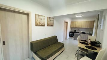 A modern living room with a sofa, a dining table with chairs, and a kitchen in the background.