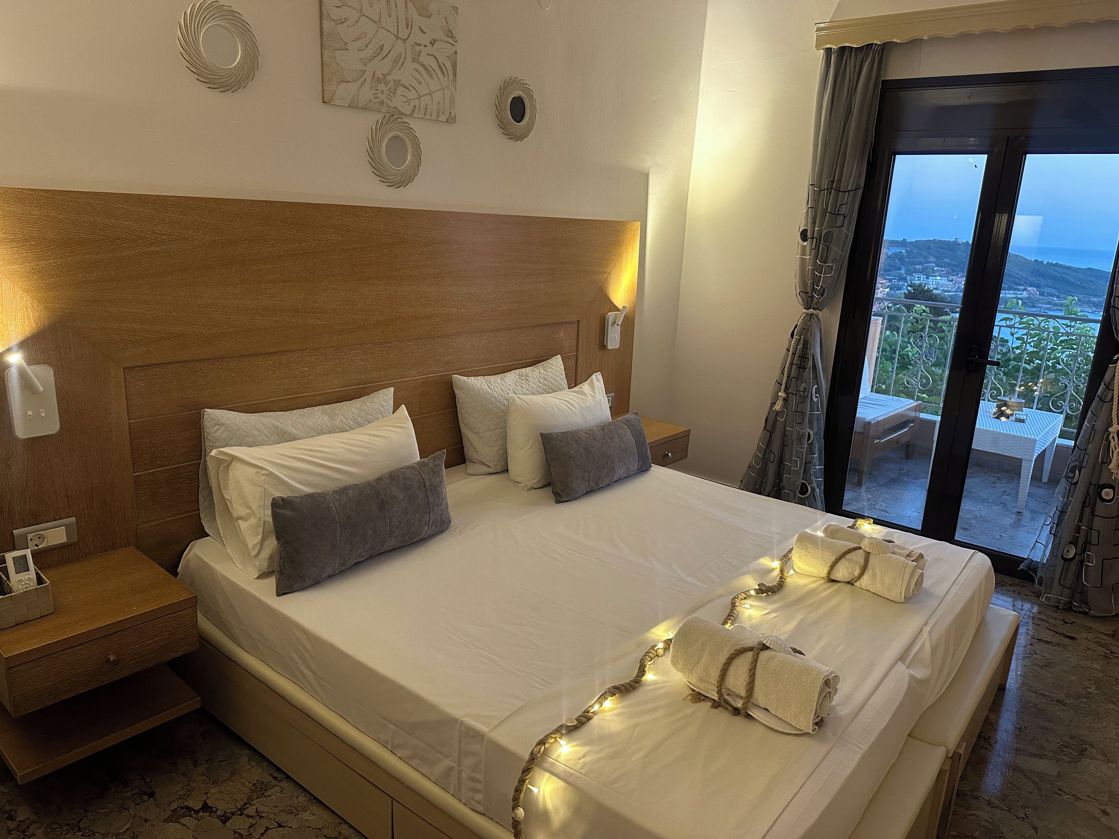 Habitación de hotel con una cama grande, cabecera de madera y vista al mar desde un balcón.