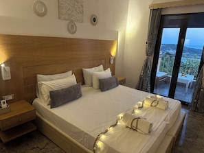 A hotel room with a large bed, a wooden headboard, and a view of the sea through a balcony. - Nikos Apartments Corfu (Corfu)