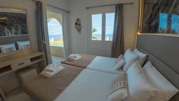 A hotel room with two beds, a desk, a mirror, and a view of the sea.