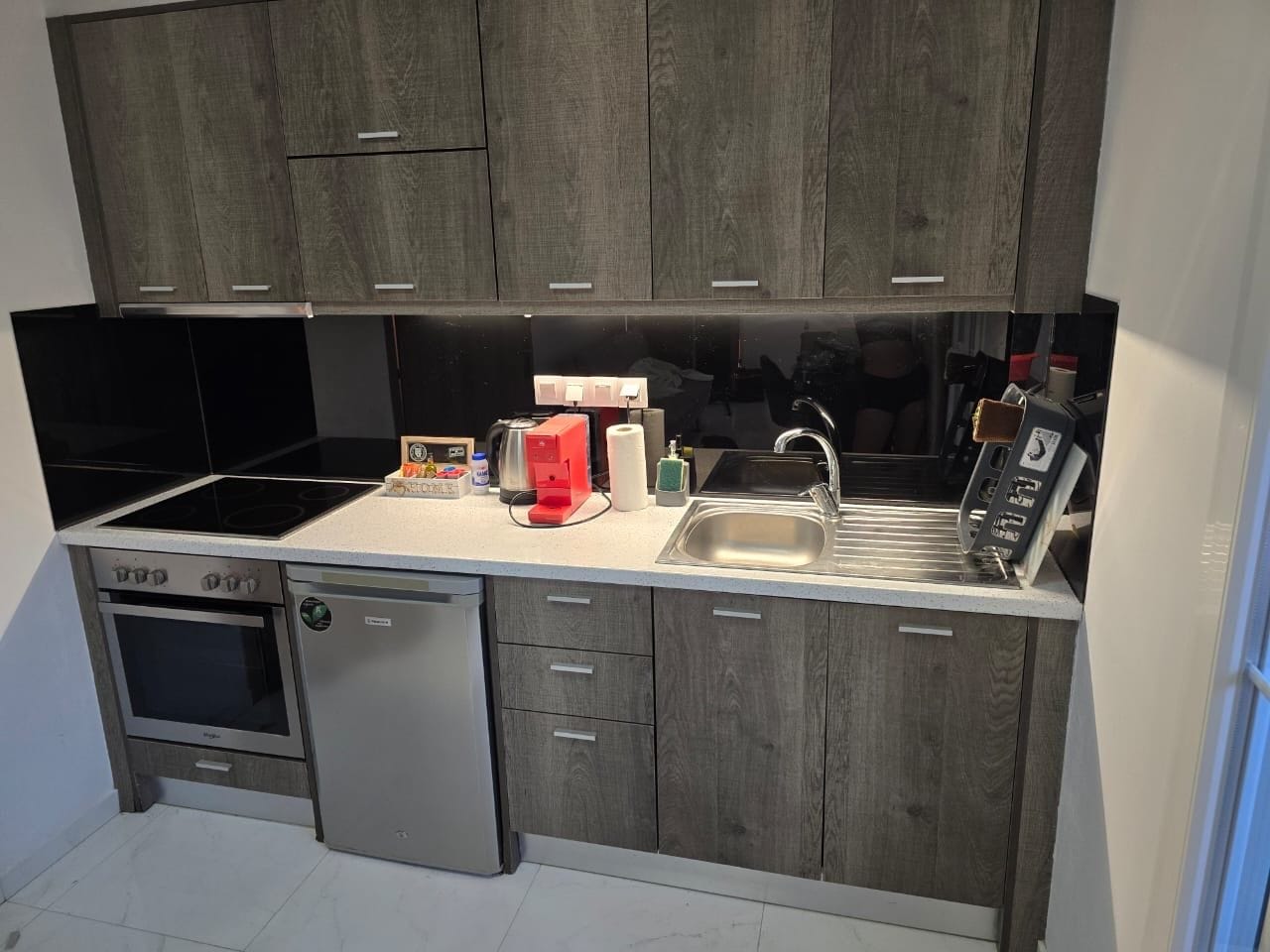 A compact kitchen with a built-in oven, a dishwasher, a sink, and a coffee maker.
