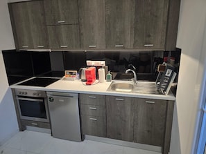 A compact kitchen with a built-in oven, a dishwasher, a sink, and a coffee maker. - Nikos Apartments Corfu (Corfu)