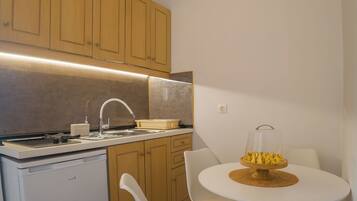 Cocina compacta con armarios de madera, encimera blanca, lavavajillas integrado y una mesa redonda con dos sillas blancas.