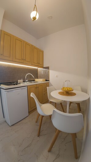 Cocina compacta con armarios de madera, encimera blanca, lavavajillas integrado y una mesa redonda con dos sillas blancas.