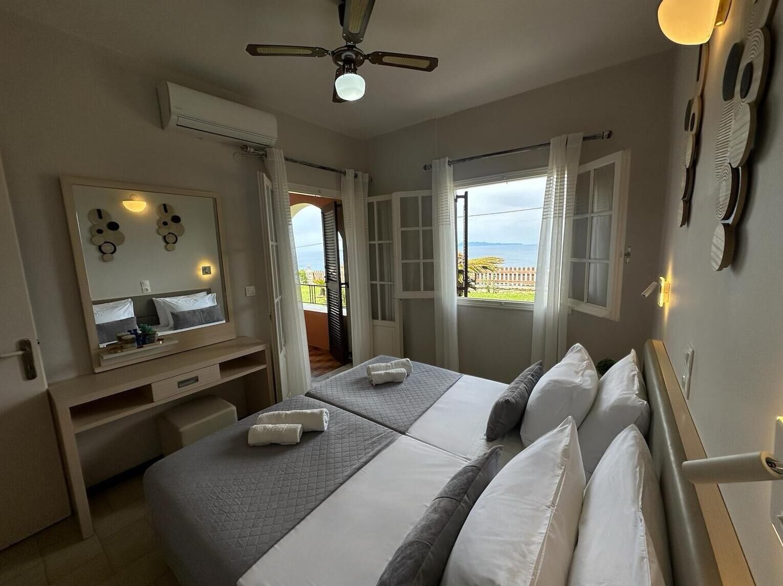 Ein Hotelzimmer mit zwei Betten, einem großen Spiegel, einem Deckenventilator und einem Fenster mit Blick.