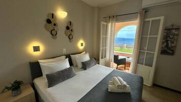 A hotel room with a bed, bedside table, wall decor, and a view of the sea through an open door.