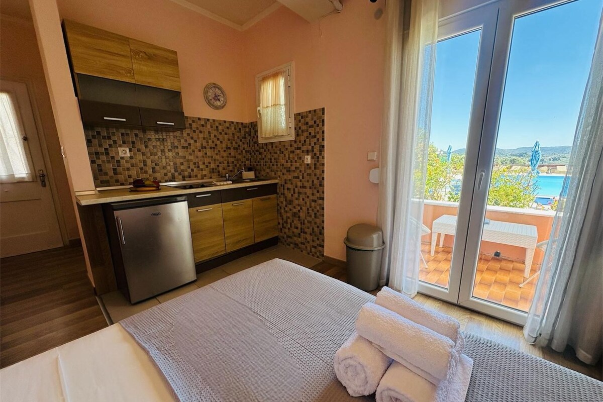 Habitación de hotel con cama, una pequeña cocina, vistas al exterior y un balcón.