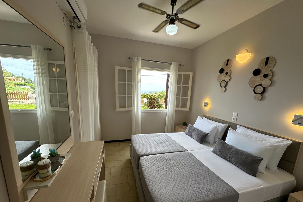 A bedroom with two beds, a ceiling fan, a window with curtains, and a view of the outdoors.