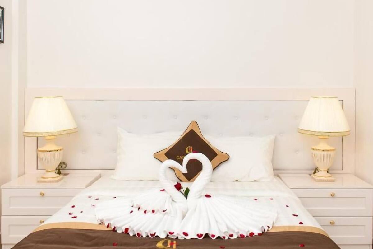 Una cama bien hecha con un arreglo de toallas con forma de cisne, una almohada decorativa y una colcha con el texto "CANHUNG".
