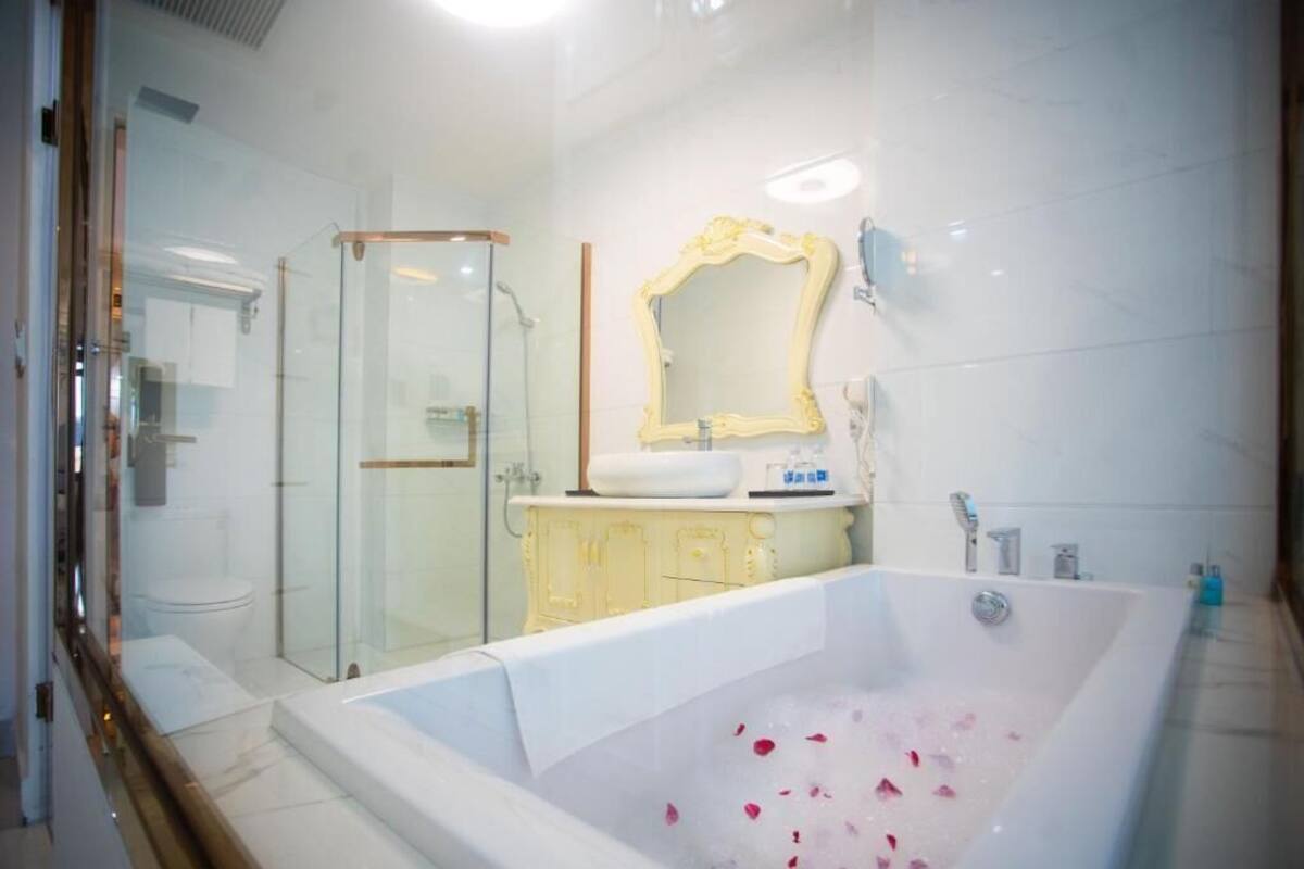 Un baño moderno con cabina de ducha de vidrio, una bañera grande con pétalos de rosa y un espejo clásico.