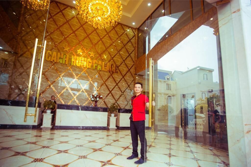 A hotel lobby with a marble floor, a reception desk, and a large chandelier.