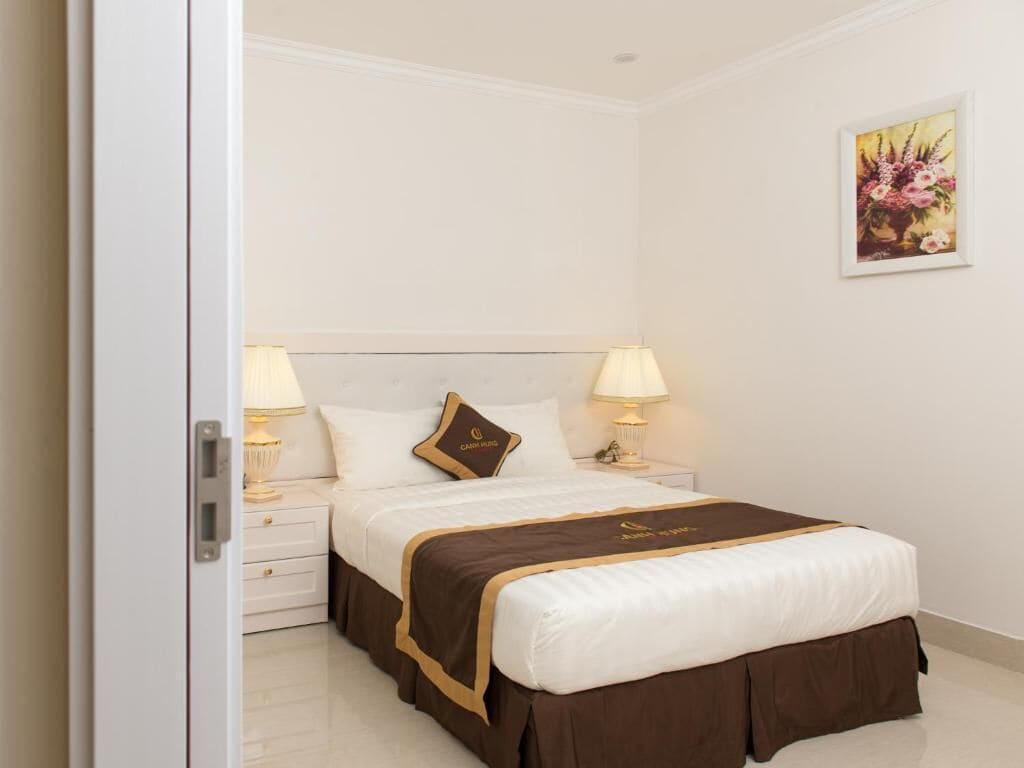 Una habitación de hotel con una cama bien hecha, dos lámparas de noche, una mesita de noche y una obra de arte floral enmarcada en la pared.