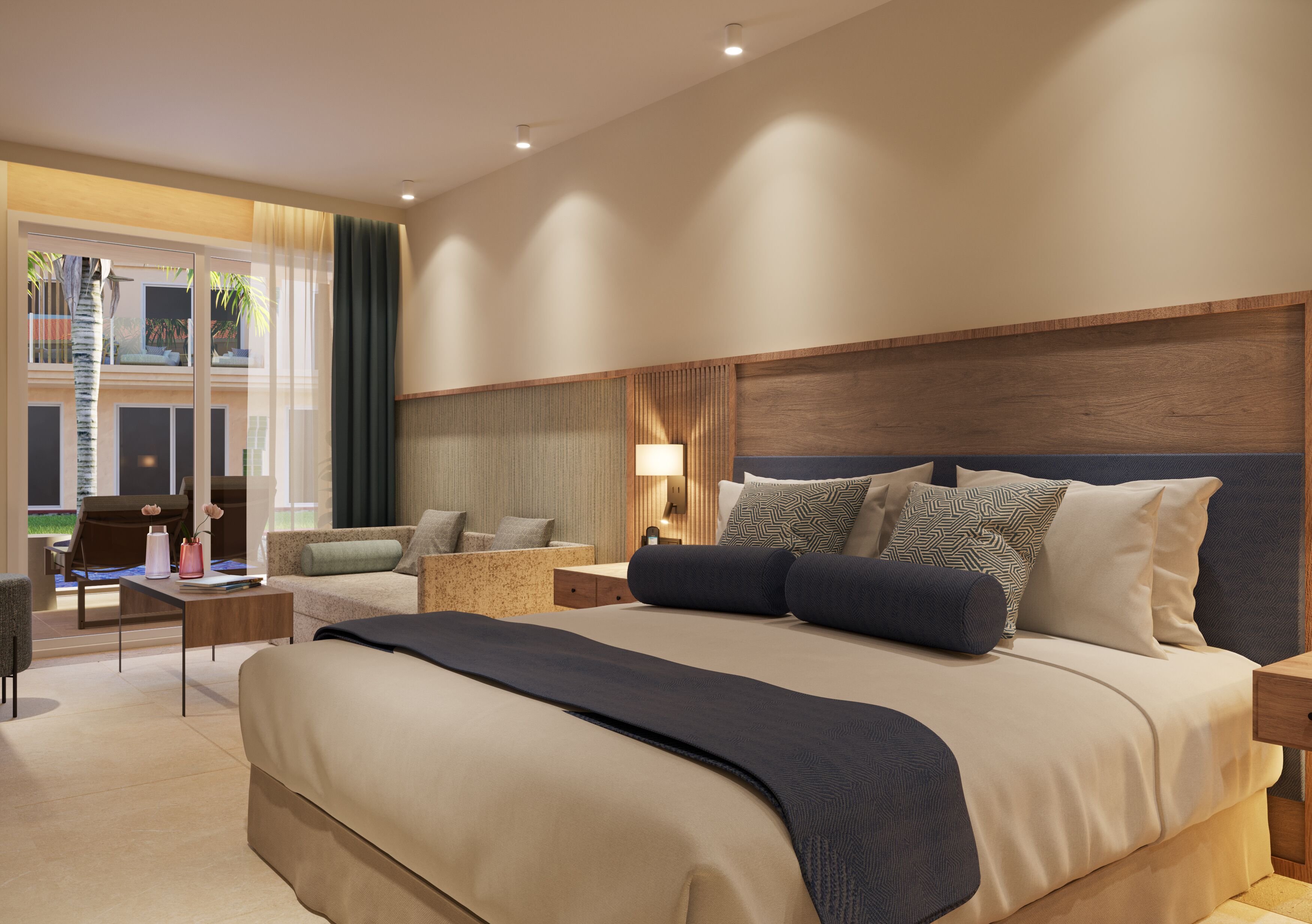A modern hotel room with a large bed, a sitting area with a sofa and armchair, a small table, and a view of the outdoors through a large window.