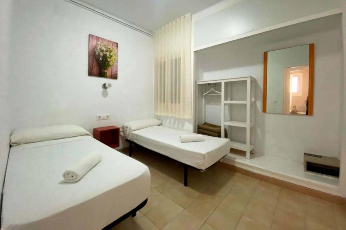 A hotel room with two single beds, a small bedside table, a wardrobe, a mirror, and a wall-mounted picture.