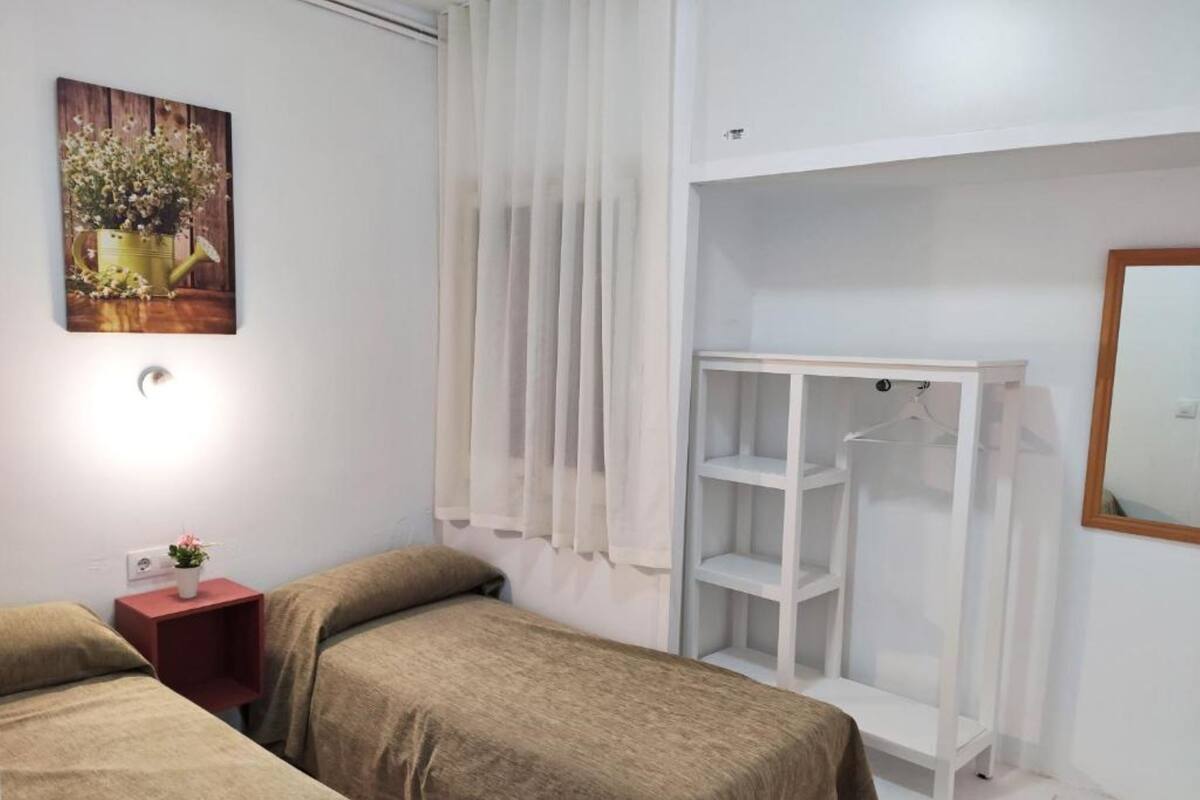 A bedroom with two beds, a white wardrobe, a small bedside table with a lamp, and a painting on the wall.