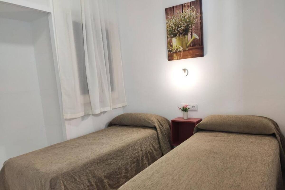 A room with two single beds, a small bedside table with a lamp, and a wall-mounted picture.