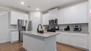 A modern kitchen with white cabinetry, stainless steel appliances, and a central island. - Spacious 4BR w/ Yard, Near Airport & F1 Circuit in Quiet Neighborhood (Austin)