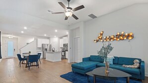 A modern living room with a teal sofa, a coffee table, and a ceiling fan. - Spacious 4BR w/ Yard, Near Airport & F1 Circuit in Quiet Neighborhood (Austin)