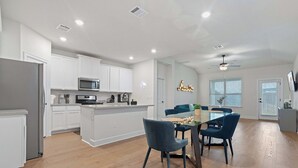 A modern kitchen with white cabinets, a microwave, and a stove. There is a dining area with a glass table and blue chairs. - Spacious 4BR w/ Yard, Near Airport & F1 Circuit in Quiet Neighborhood (Austin)