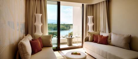 A modern hotel room with a large window, a sofa, a coffee table, and a view of a body of water.