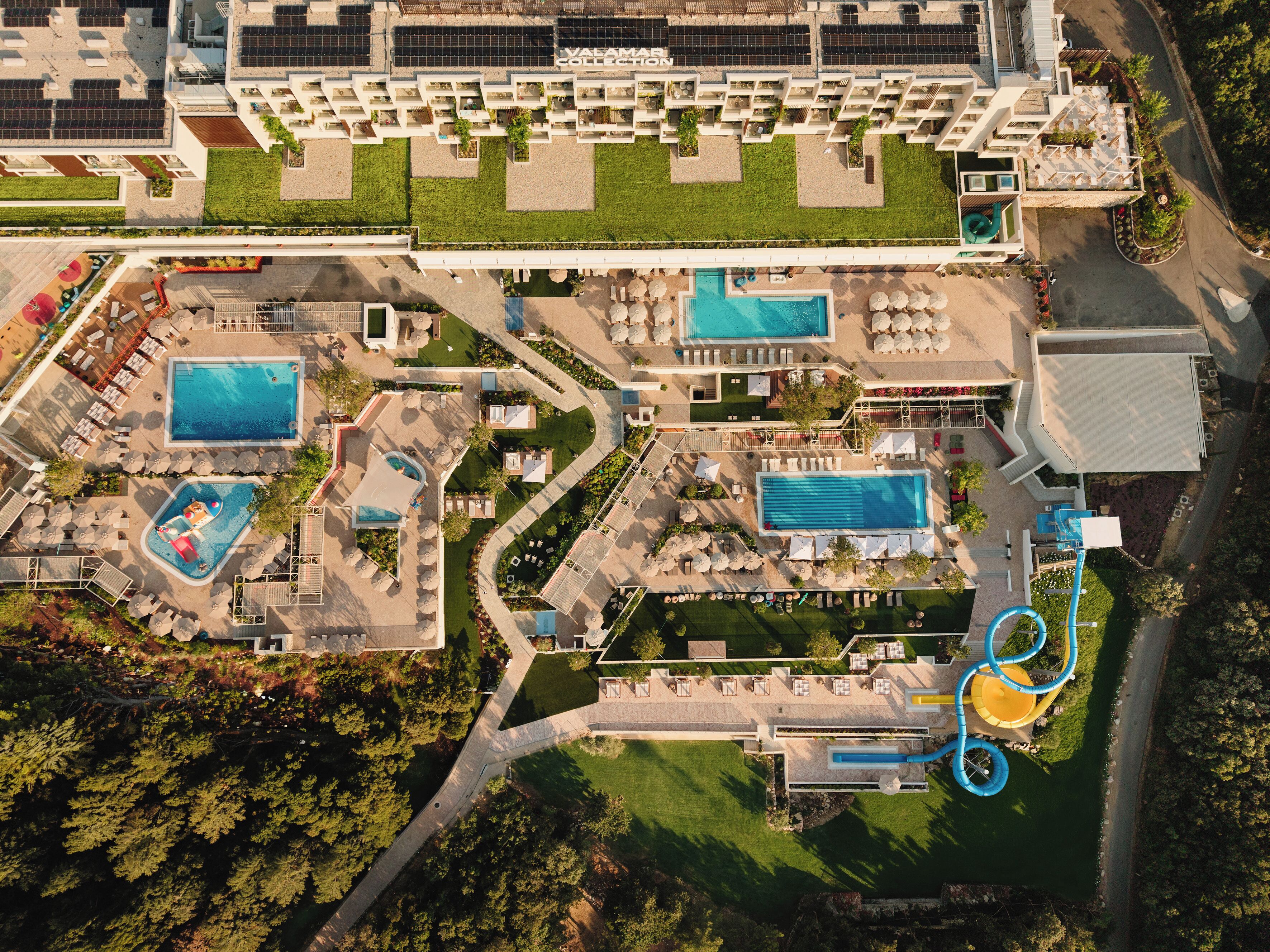 Vue aérienne d’un complexe hôtelier doté de plusieurs piscines, de chaises longues et d’un toboggan aquatique.