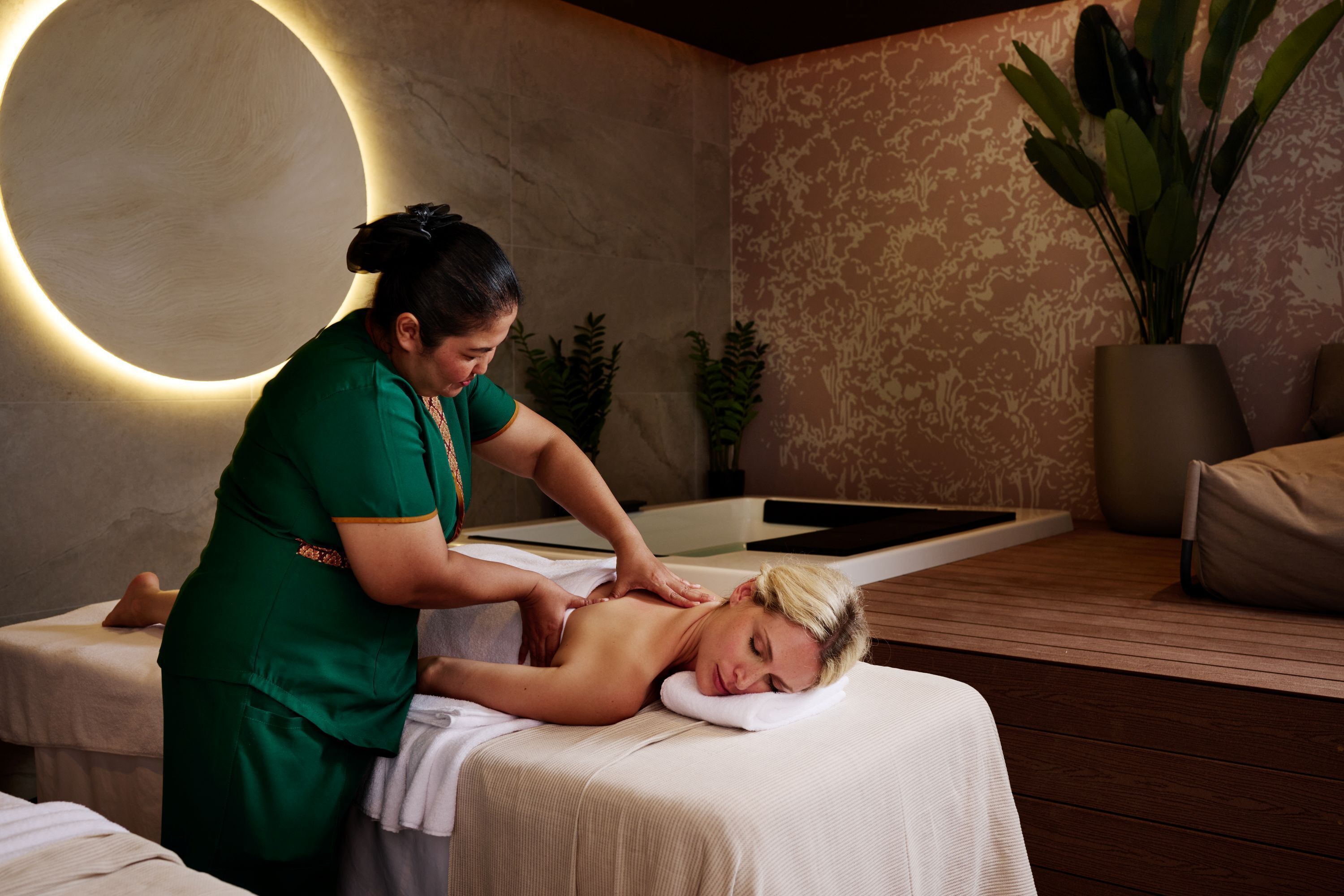 A massage therapy room with a wooden floor, a massage table, and a wall-mounted massage light.