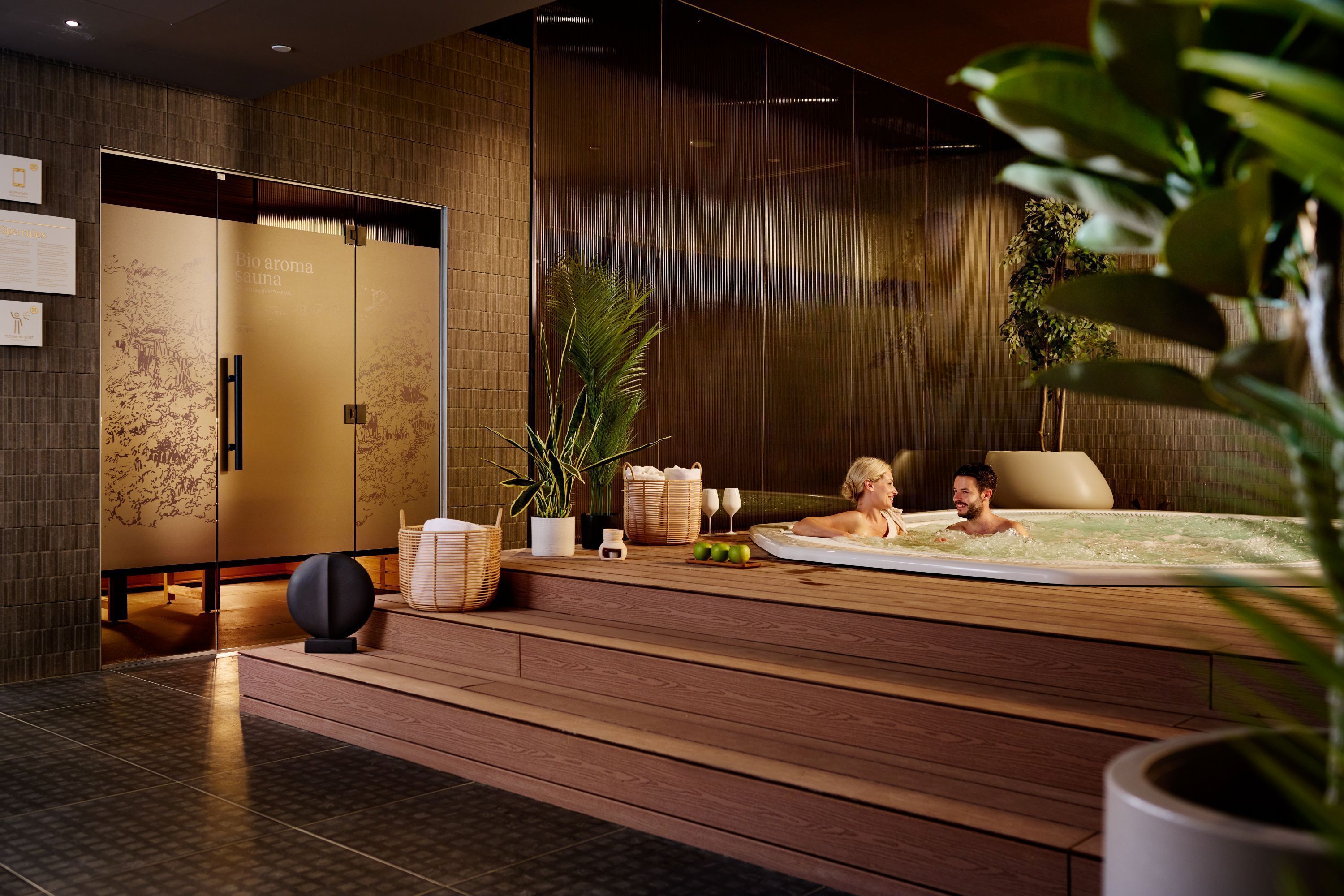 A modern spa area with a hot tub, wooden flooring, and a large potted plant.