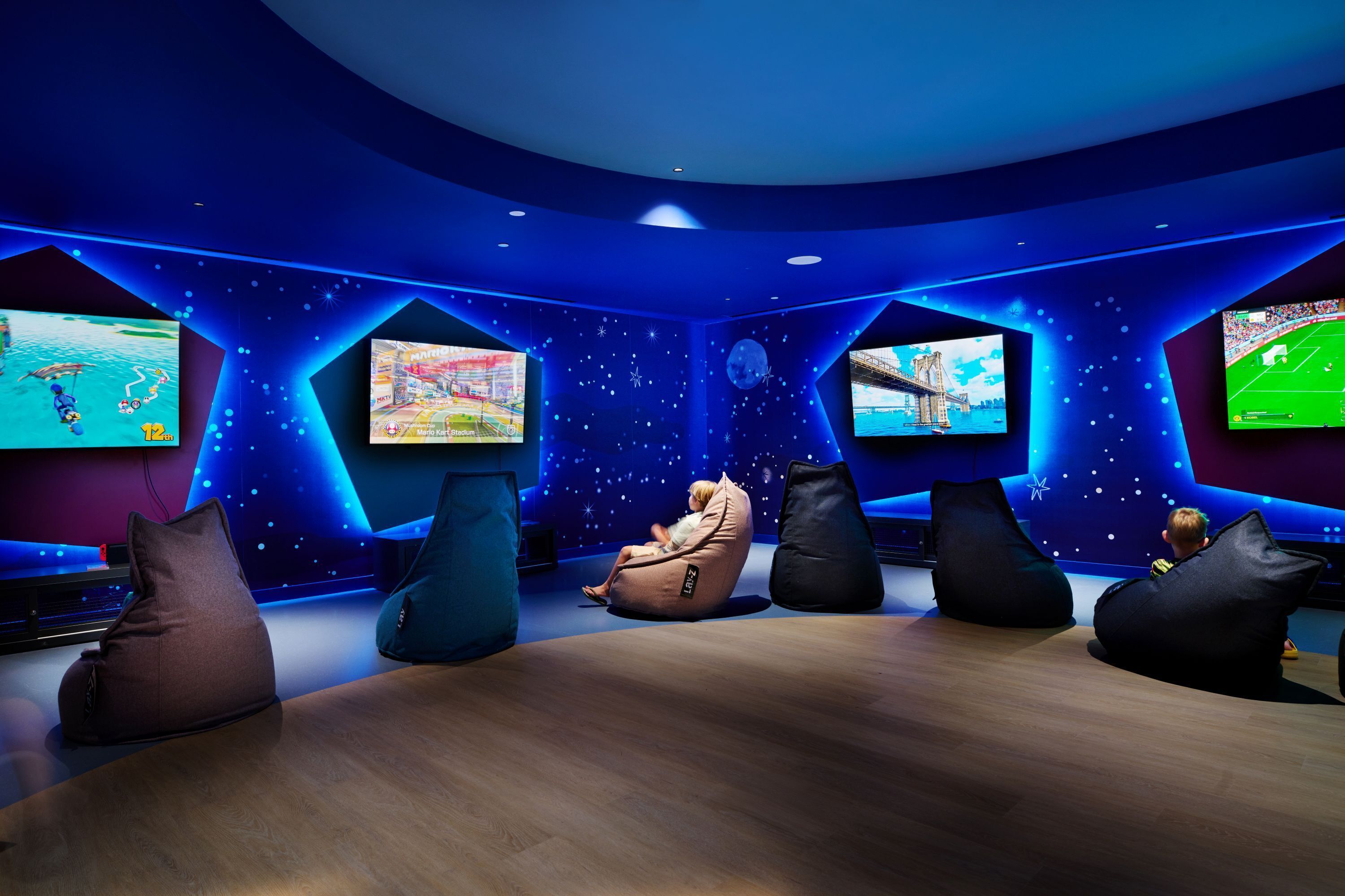A room with hexagonal screens displaying various games, bean bags, and a wooden floor.
