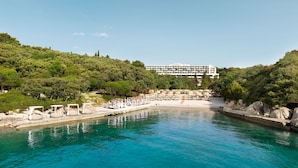 A coastal hotel with a pool, beach chairs, and a view of the sea.