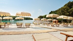 A beach with rows of sun loungers and umbrellas, a wooden deck, and a view of the sea.