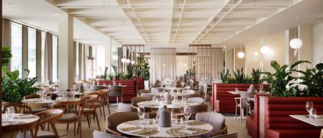 A spacious restaurant with round tables, wooden chairs, and red booths.