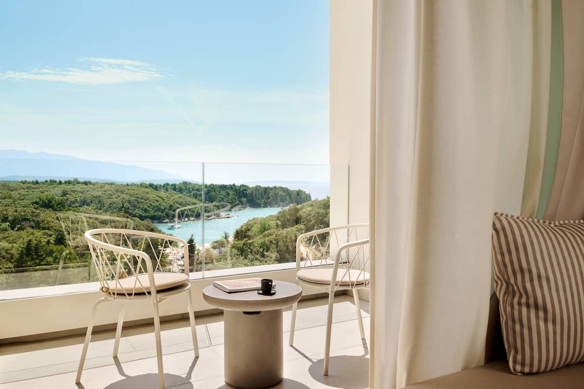 A balcony with two white chairs, a small round table, and a view of a coastal landscape.